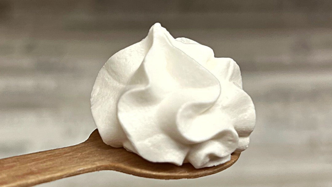 Meringa senza uova IN-VECE montata con aquafaba, dressata su un cucchiaio di legno