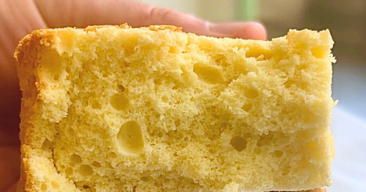 Fetta di Pan di Spagna senza uova IN-VECE tenuta in mano, con la mollica alveolata e il colore giallo in primo piano