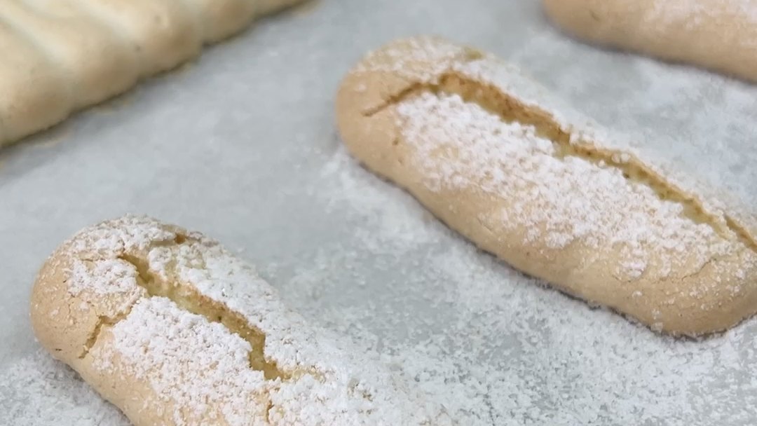 Savoiardi senza uova IN-VECE spolverati di zucchero a velo su carta forno, appena sfornati